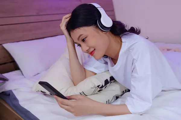 Smiling girl in headphones watching funny videos on smartphone
