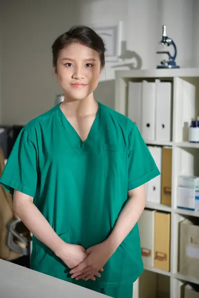 Portrait of positive veterinary nurse in green scrubs staning in medical medical office