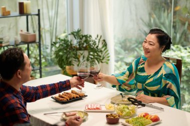 Neşeli Bay Vietnamlı çift evde romantik bir akşam yemeği yiyor. Şarap kadehleriyle kadeh kaldırıyorlar.