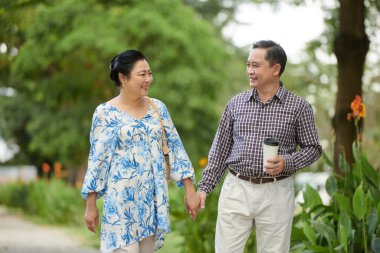 Gülümseyen kıdemli karı koca işten sonra şehir parkında yürüyor.