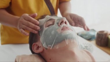 Güzellik salonunda kadın güzellik uzmanının erkek yüzü maskesini kapamak rahatlatıcı.