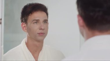 Banyoda aynanın karşısında duran, yüzünü temizleyici köpükle yıkayan genç bir adamın omzunda.