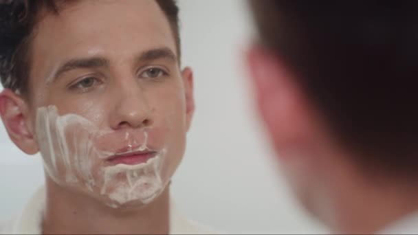 男人一边用剃须刀刮脸一边站在镜子前准备早上的工作 — 图库视频影像