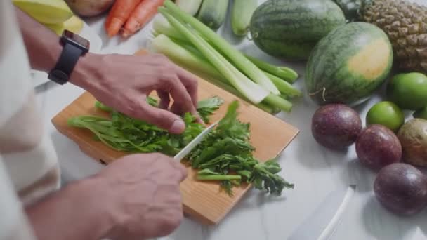 キッチンで健康的な朝食のためにスムージーやサラダを準備する木製ボード上の認識できない男性料理の切削緑の手の近く — ストック動画
