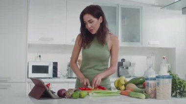 Yeşil iç çamaşırlı, sebze salatası yapan beyaz bir kadının dijital tabletten tarifine bakarken orta boy fotoğrafı.