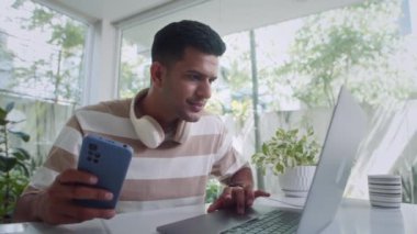 Akıllı telefon ve dizüstü bilgisayar kullanan serbest çalışan erkek çalışanların odak noktası rahat oturma odasında, ağır çekimde oturuyor.