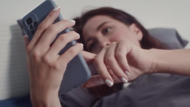 Rack Focus Van Jonge Vrouw Scrollen Feed Smartphone Liggend Bed — Stockvideo