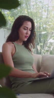 Kanepede otururken dizüstü bilgisayarda çalışan beyaz kadın girişimcinin dikey görüntüsü.