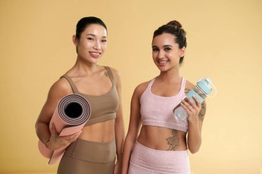 Yoga minderi ve su şişesiyle mutlu, formda genç kadınların portresi.