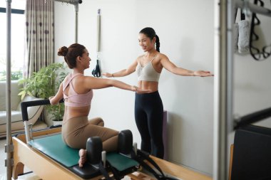 Mutlu koç müşteriye özel makinede egzersiz yaparken kollarını düz tutmasını söylüyor.