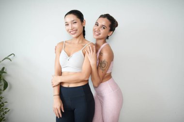 Spor sutyenli ve taytlı mutlu kızlar spor salonunda duvara yaslanıyor.
