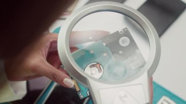 Servis merkezindeki büyüteçten bozuk hard diske bakan bir uzman.