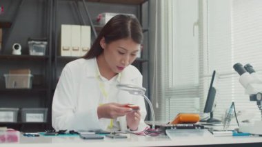 Servis merkezinde çalışırken cep telefonu tutan ve kameraya bakan neşeli kadın teknisyenin orta boy portresi