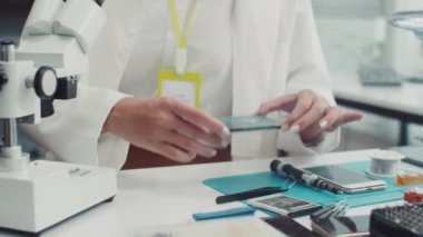 Bozuk telefon detaylarını mikroskop altında inceleyen beyaz işçi kadın uzmanının orta boy fotoğrafı.