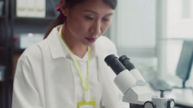 Beyaz işçi kıyafetli kadın bilim adamının portresini mikroskop kullanarak yukarı kaldır ve kameraya gülümse.