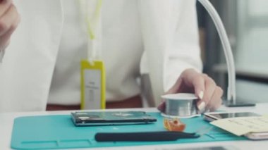 Kadın teknisyen, servis merkezindeki büyüteçle elektronik tamir yapıyor.