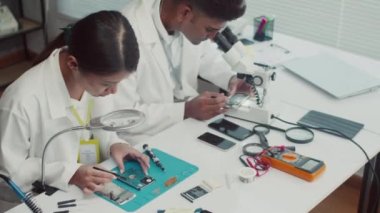 Servis merkezinde çalışan beyaz önlüklü teknisyenlerin yüksek açısı mikroskop ve tamir için büyüteç kullanıyorlar.