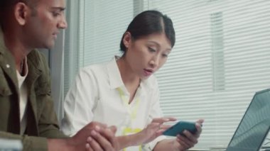 Tamirci kadının servis merkezinde dizüstü bilgisayarın önünde oturan akıllı telefonu ayarlayan erkek müşteriye yardım ederken orta boy fotoğrafı.
