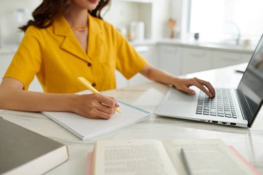 Öğrenci laptopta eğitim videosu seyrediyor ve defterde yazıyor