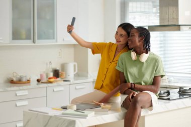 Mutfak adasında oturan neşeli kızlar sosyal medya için selfie çekiyorlar.