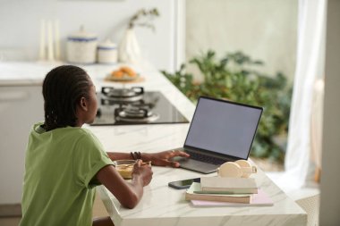 Siyah kız kahvaltı yapıyor ve dizüstü bilgisayardan eğlenceli videolar izliyor.