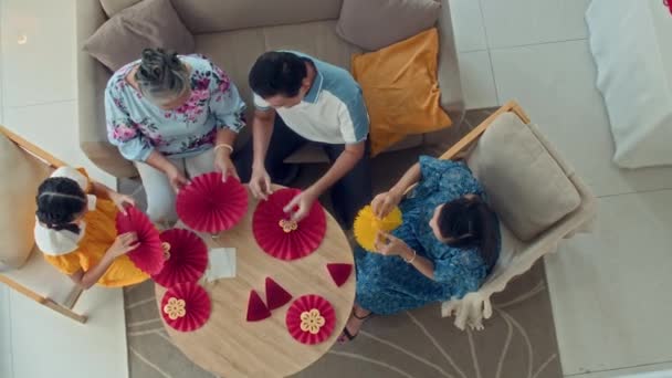 自宅でテトのお祝いのための装飾を作っている間 円卓に座っている多世代のアジアの家族の直接の眺め — ストック動画