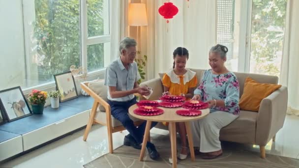 祖父母和少女坐在圆桌边 为农历新年制作红纸装饰品的长镜头 — 图库视频影像