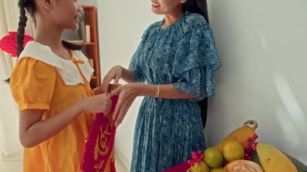 黄色いドレスで陽気な十代の少女と彼女の母親がテトのお祝いのために準備する壁に赤い紙の装飾をぶら下げたショット — ストック動画