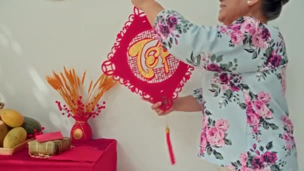 自宅でテトを祝う壁に装飾でベトナムの伝統的な装飾を吊るす祖母と孫娘のショットを傾けました — ストック動画