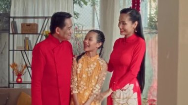 Mutlu Vietnamlı ebeveynlerin portresi genç kızlarına sarılıyor ve Tet kutlamaları sırasında kameraya bakıyor.