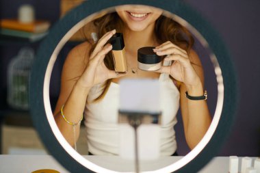 Gülümseyen kız güzellik blogu çekerken abonelerine fondöten ve yüz pudrası gösteriyor