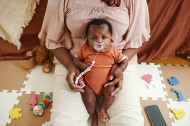 Sevimli siyah yeni doğmuş bebek emzik emziren annenin ellerinde ve kameraya bakıyor.