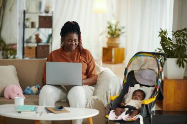Gülümseyen siyah kadın bebeği uyurken internetten ders çalışıyor.