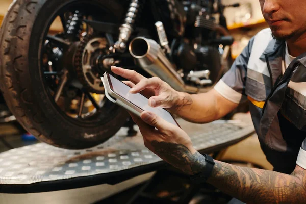 Cropped image of repairman checking scheme of motorcycle on tablet computer
