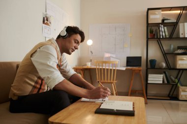 Bina planlarını düzeltirken kulaklıkla müzik dinleyen inşaat mühendisi