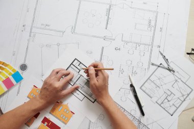 Mimarın elleri ofis masasındaki kat planlarını düzeltiyor, yukarıdan bakıyor.