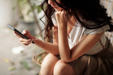 Uzun saçlı, akıllı telefondan mesajları kontrol eden genç bir kadının kırpılmış görüntüsü.