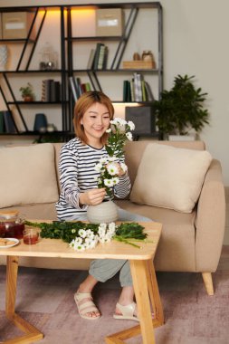 Gülümseyen genç Asyalı kadın evde papatya çiçekleri düzenliyor.