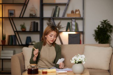 Kişisel mali işleriyle ilgilenen, faturalarını ve maaş çeklerini kontrol eden ciddi genç bir kadın.