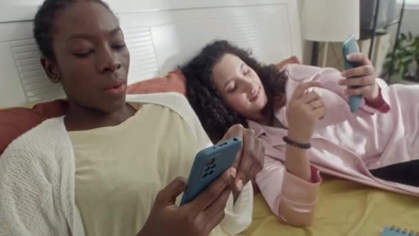 在租来的公寓里躺在床上时 有两个女孩在智能手机上滚动喂食 这是个中等特写镜头 — 图库视频影像