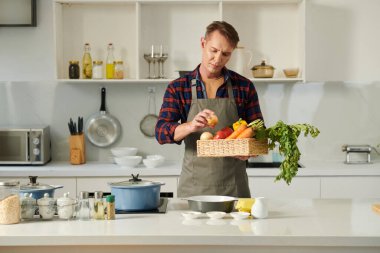 Kaşlarını çatan olgun adam evde pişirdiği en iyi sebzeyi seçiyor.