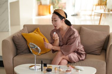 Ruj sürerken büyüteç aynasına bakan genç bir kadın.