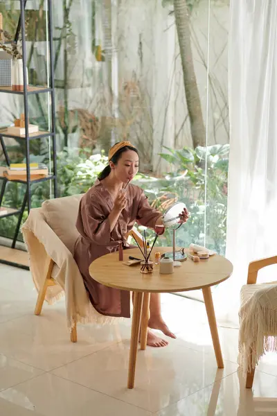 Chinese young woman in satin robe doing makeup when getting ready in the morning