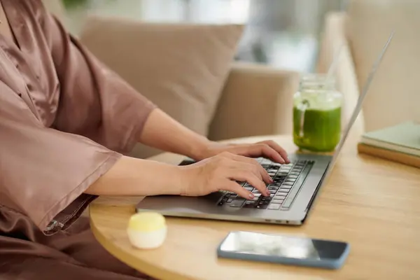 Woman in silk robe working on laptop and drinking morning smoothie