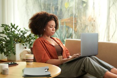 Evdeki kanepede oturup rapor üzerinde çalışan konsantre Latin kadının portresi.