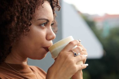 Düşünceli Latin kadın sabah kahvesini içiyor ve balkonundan şehre bakıyor.