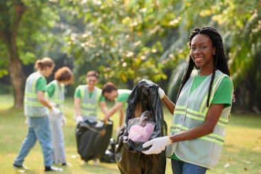 Bir çanta dolusu plastik çöpü gösteren neşeli bir çevre gönüllüsünün portresi.