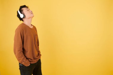 Genç adam en sevdiği şarkıyı kulaklıkla dinlerken başını arkaya yaslıyor.