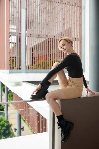 时尚的年轻女子坐在阳台栏杆上 看着镜头 — 图库照片