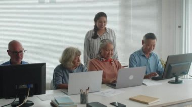 Geniş açı, bilgisayar dersi sırasında çeşitli son sınıf öğrencilerinin ilerlemelerini kontrol eden genç bayan öğretmenler.